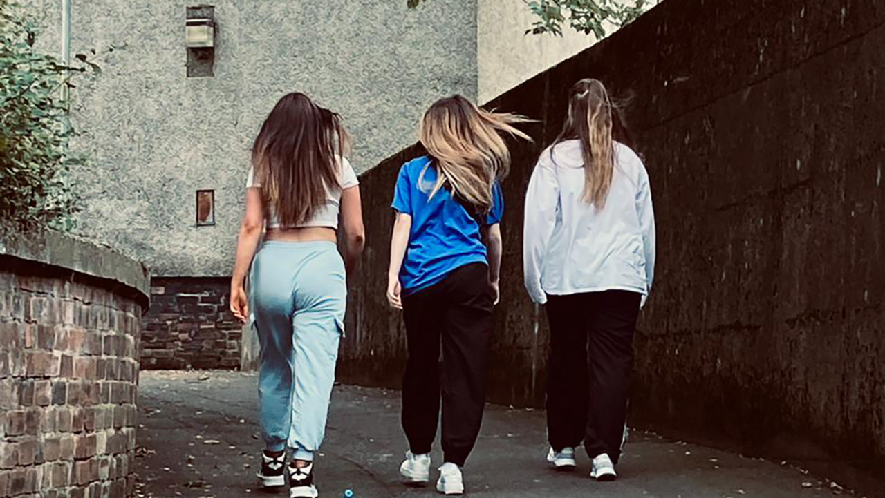 Three young woman walk away from the camera up an alley.